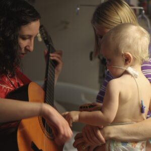 Woman playing guitar with baby and mother